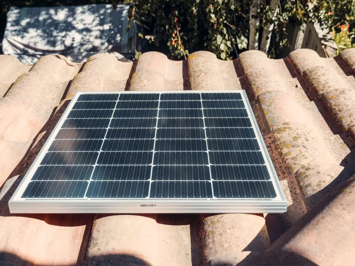 A solar panel fixed on a clay-tiled roof in sunlight